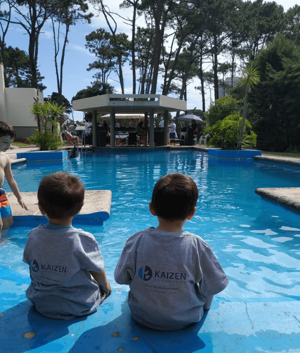 A photo of two children sitting at the edge of a pool wearing Kaizen Softworks t-shirts, enjoying a relaxing moment by the water