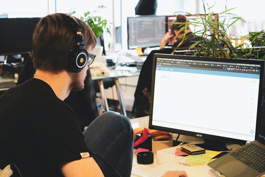 An image of a focused man wearing headphones, coding on a computer.