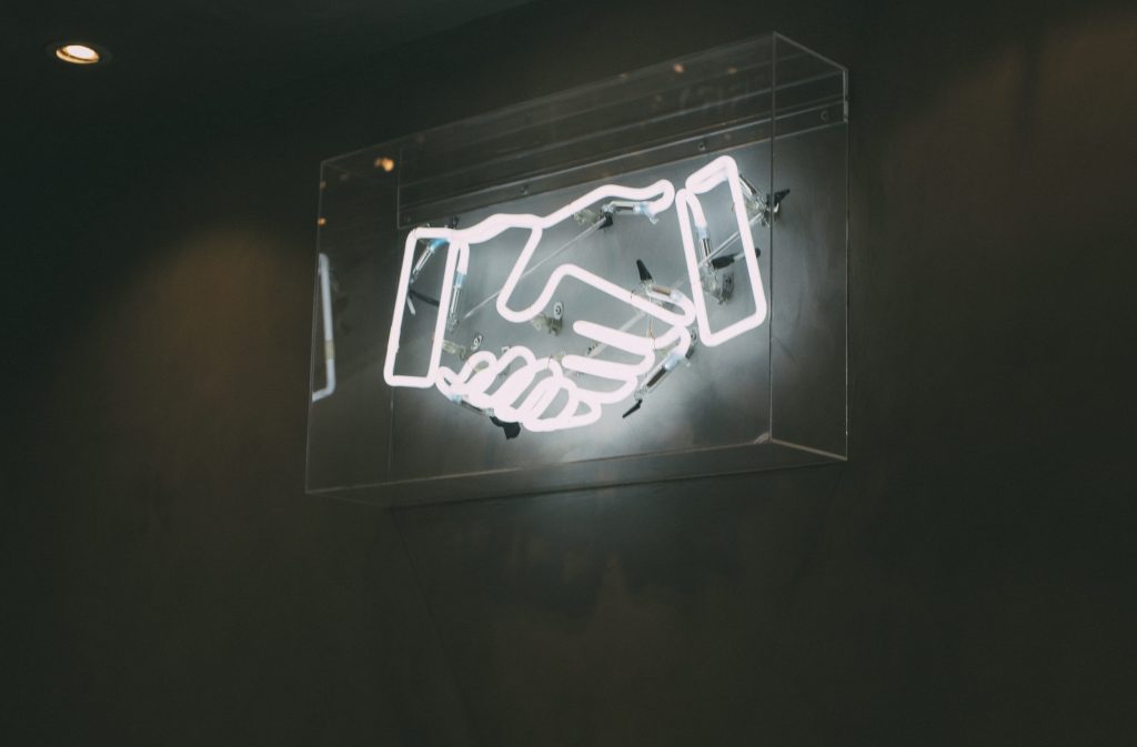 Image of a neon sign portraying a handshake, symbolizing a strong partnership.