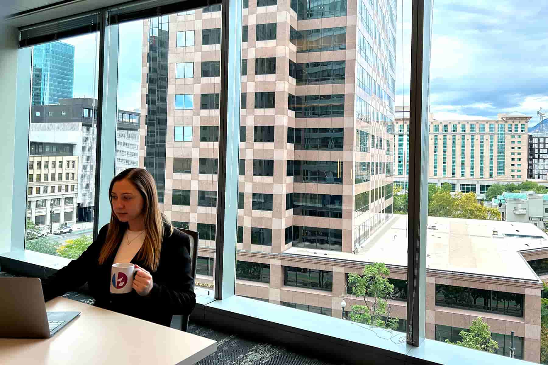 A photo featuring Valentina enjoying a cup of coffee in the Kaizen Softworks Salt Lake City office, with a scenic view of the cityscape visible through the office window.