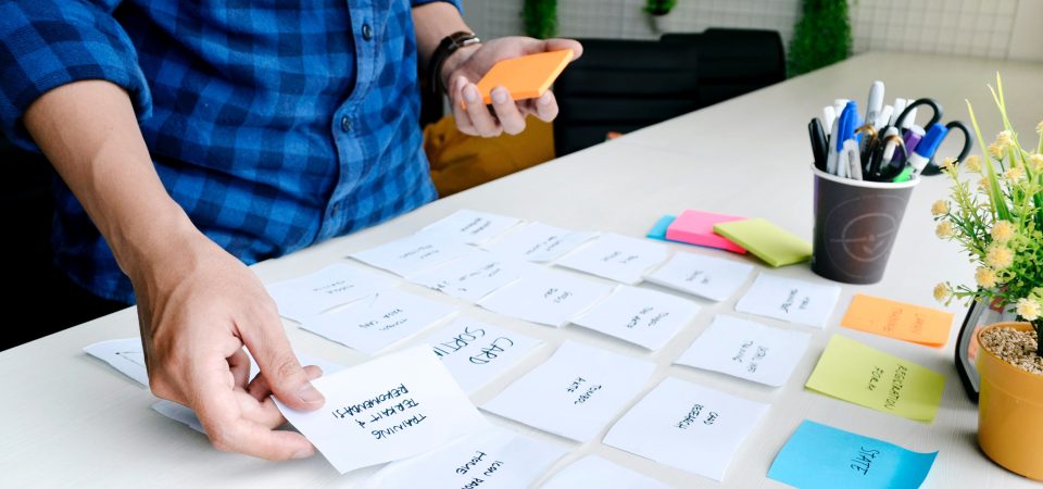 A person strategically placing sticky notes on a table, symbolizing the Agile methodology and thoughtful assessment of options for effective decision-making.