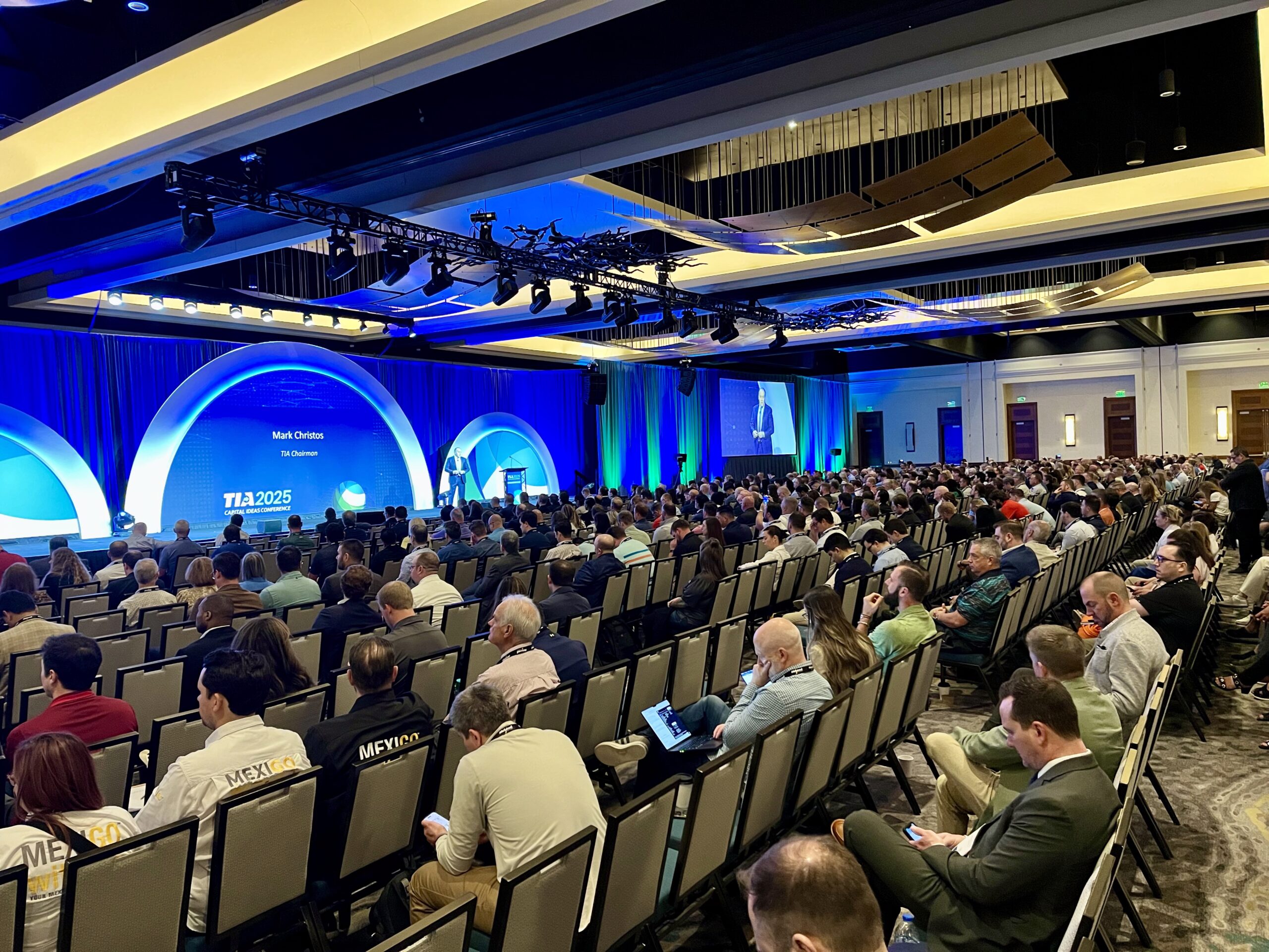 Large audience at TIA 2025 conference listening to a presentation on stage with blue lighting.