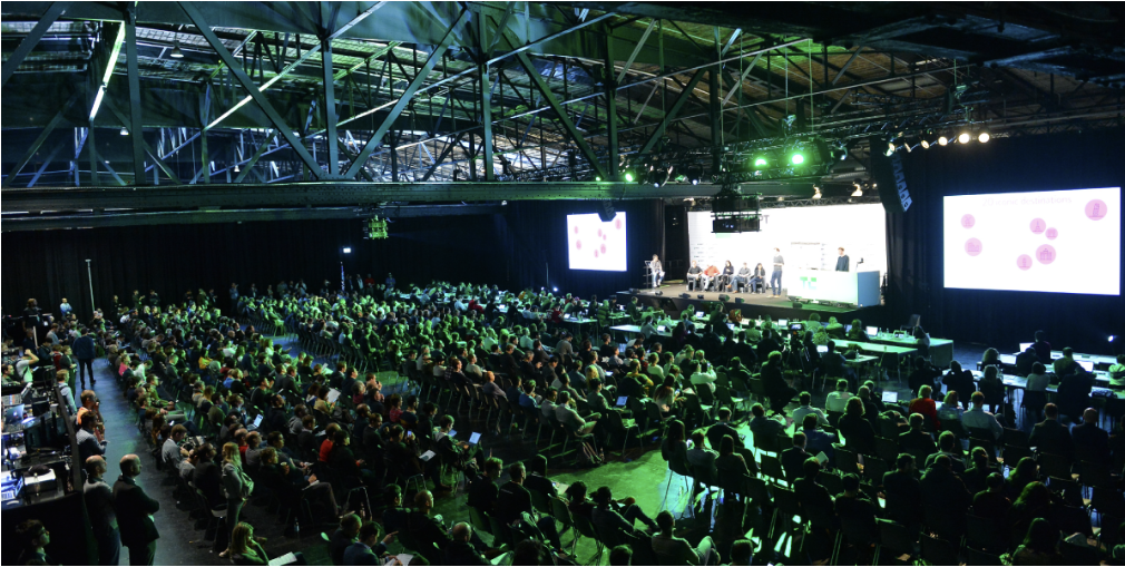 Crowd attending a talk at a past edition of TechCrunch Disrupt, a major U.S. tech startup event, with large screens on stage.